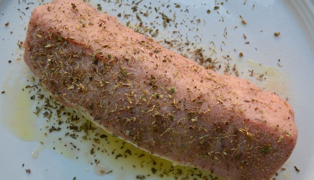 un rôti de porc cru sur lequel on a badigeonné une marinade aux herbes